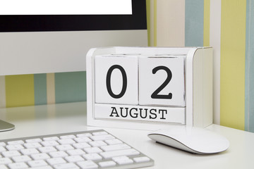 Cube shape calendar for AUGUST 2 and computer with white screen on table. 