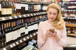 © Zoriana - Woman using her smart phone at the wine supermarket