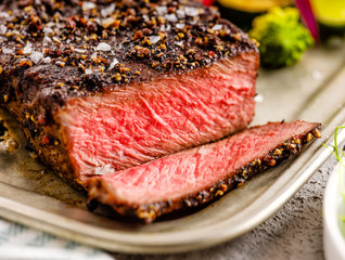 A grilled pepper steak garnished with lemon, onion and fresh herbs