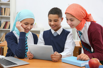 Schoolchildren using tablet at desk in classroom