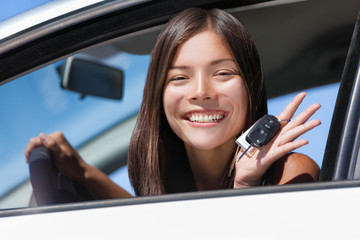 Wall Mural - Happy Asian girl teen driver showing new car keys. Young woman smiling driving new car holding key. Interracial ethnic woman driver holding car keys driving rental car.