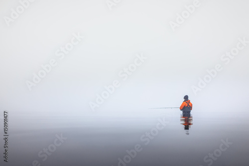 Angler in Wathose im Wasser am Meer bei Nebel an der Küste