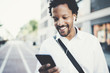 © SFIO CRACHO - Closeup view of Attractive american african black man listening to music with headphones in urban background. Happy men using smartphone outdoors.Flares effects, blurred background.