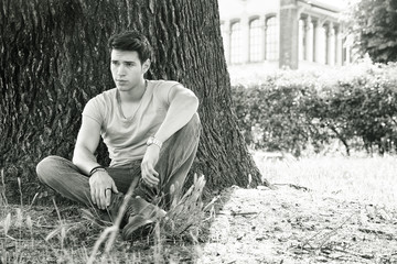 Wall Mural - Attractive young man in park resting or relaxing against tree, in a sunny summer day