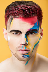 Wall Mural - portrait of young man with colored face paint on yellow background. Professional Makeup Fashion. fantasy art makeup