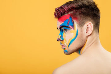 Wall Mural - portrait of young man with colored face paint on yellow background. Professional Makeup Fashion. place for text