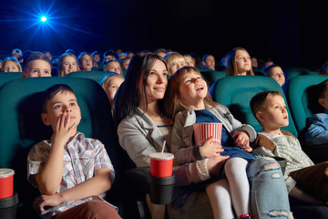 Low angle shot of people watching a movie at the cinema. Young woman and her daughter enjoying a film at the movie theatre motherhood parenting children kids entertaining happiness.