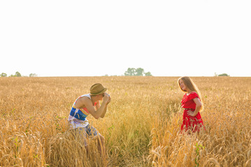 photographer with camera taking picture of young beautiful woman in the field.