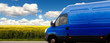 Transporter fährt auf einer Landstraße mit Rapsfeld und blauem wolkigen Himmel mit Sonne