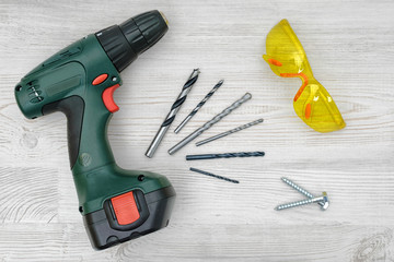 Wall Mural - A cordless drill set on a wooden table background with a set of bits in the box and yellow protective glasses around.