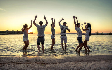 Silhouette of group young people on the beach under sunset sky w