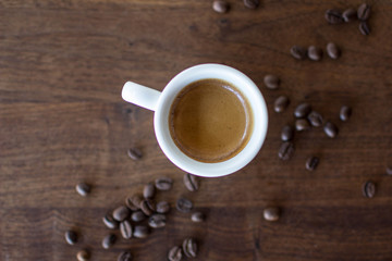 Freshly brewed espresso surrounded by coffee beans on a warm walnut wood table 