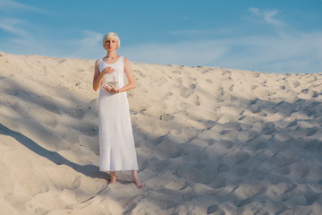 Wall Mural - Young tender beautiful blonde woman in the desert with goldfish in her hands 