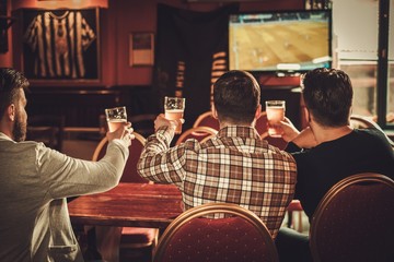 Wall Mural - Cheerful old friends watching sports and drinking draft beer in pub.