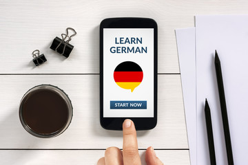 Wall Mural - learn german concept on smart phone screen with office objects on white wooden table. all screen con