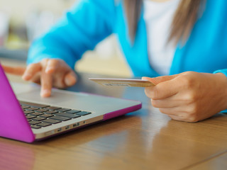  Pretty Young womans hands holding a credit card and using laptop computer for online shopping. Online payment. Female working on laptop in a cafe.