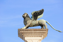 Close-up Of Column With The Winged Lion, Symbol Of Venice, And Blue Sunny Sky In Piazza San Marco. At The City Of Venice, The Historic And Amazing Marine City.