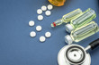 stethoscope, pills, vials in medical room on blue background