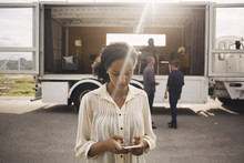 Businesswoman Using Smart Phone With Colleagues And Portable Office Truck In Background