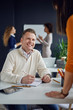 © nenadaksic - Young man is talking to his colleague in the office, two women discuss behind him in front of whiteboard