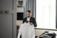 Businessman Holding White Shirt In Coathanger Against Window At Hotel Room