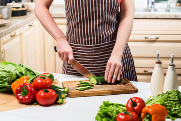 Young woman cooking in the kitchen at home. A woman cuts a cucumber and vegetables with a knife.