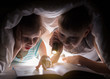 © Alfira - Children bedtime. Sister and brother are reading a book under a blanket with flashlight. Pretty young boy and lovely girl having fun in children room.