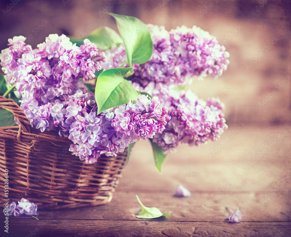 Lilac flowers bunch in a basket over blurred wood background - obrazy, fototapety, plakaty 