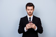 © deagreez - Serious minded man in black suit holding smartphone and typing sms on it