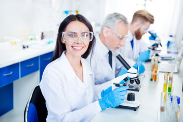 Success in inventing new technology! Young lab worker is smiling and her colleagues are working for experiment. They have all modern equipment they need