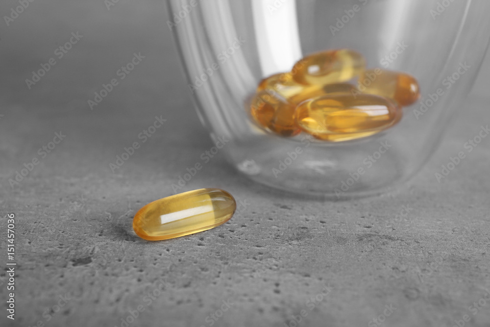 Glass with fish oil capsules on grey background