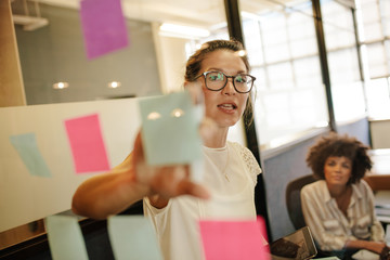 Wall Mural - Businesswoman pointing at sticky note to colleague