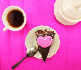 Chocolate cake on a rose background with milk chocolate and heart top. Love to sweet. Symbol of sweet tooth and lovers of cakes, sweets and cookies. Sweet breakfast