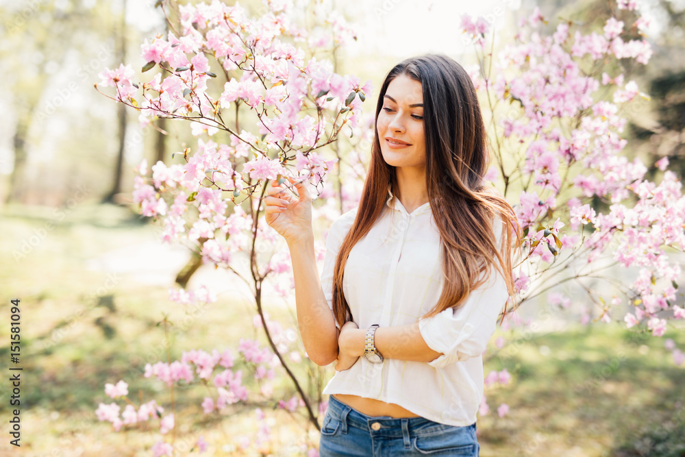 Outdoor portrait of a young beautiful woman near magnolia tree with flowers.