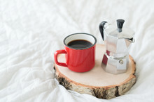 Red Metal Mug Of Coffee With Steel Coffee Maker On White Bed