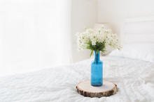 Flowers In Blue Bottle Flower Pot On Bed With Copyspace In White Interior