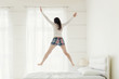 © Demetrio - Rear view of young woman jumping up on bed at home