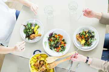 Wall Mural - Top view of two young women eating green salads with chiken and potato