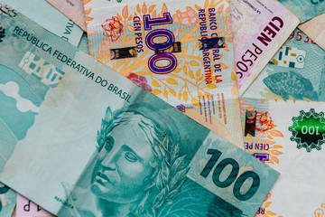 Macro close-up of 100 Brazilian reais over 100 Argentine peso bills