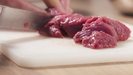 Wall Mural - Slow motion slide shot of young female hand cutting raw beef with a knife on plastic board, 180fps prores footage