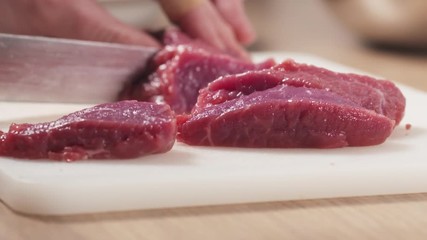 Wall Mural - Slow motion slide shot of young female hand cutting raw beef with a knife on plastic board, 180fps prores footage