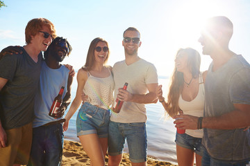 Wall Mural - Laughing friends in sunglasses having rest by seaside