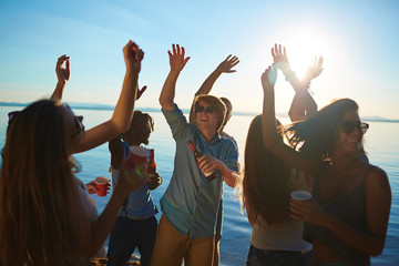 Wall Mural - Dynamic guys and girls dancing with drinks on the beach