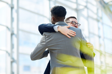 portrait of two business partners hugging and smiling with happiness standing in modern glass hall o