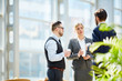 © pressmaster - Group of business people discussing work during coffee break  standing in modern glass hall of office building