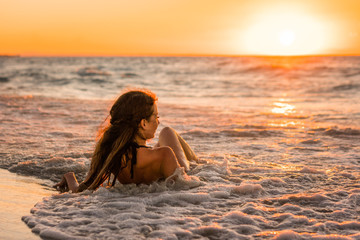 Wall Mural - Beautiful young woman with long brunette hair in black swimsuit lies a back on the sand of caribbean coastline