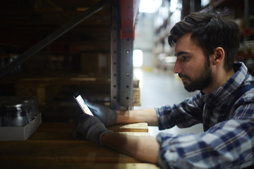 Wall Mural - Distribution department manager with smartphone leaning on shelf with packed products