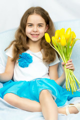 Beautiful blond schoolgirl with yellow tulips sitting on the cou