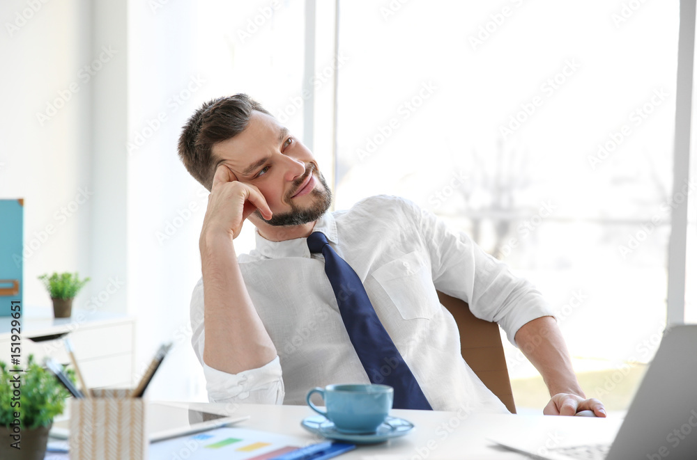Young businessman relaxing at workplace with cup of coffee