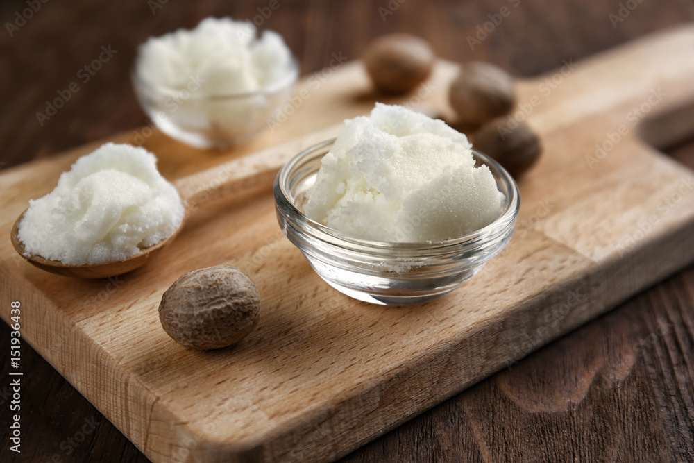 Shea butter in bowl and spoon on wooden background